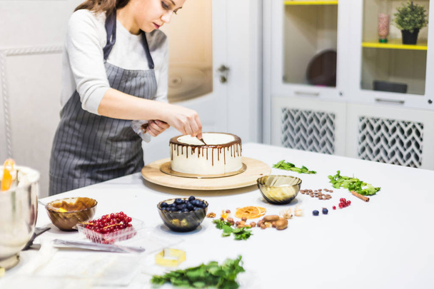 A confectioner squeezes liquid chocolate from a pastry bag onto a white cream biscuit cake on a wooden stand. The concept of homemade pastry, cooking cakes. - Foto, immagini