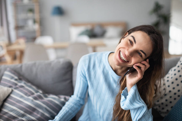 Attractive smiling woman talking on the phone while sitting on the sofa. - Zdjęcie, obraz