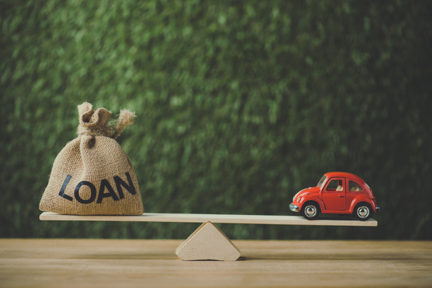 carro em miniatura vermelho e saco de dinheiro com palavra empréstimo balanceamento em seesaw no fundo verde
 - Foto, Imagem