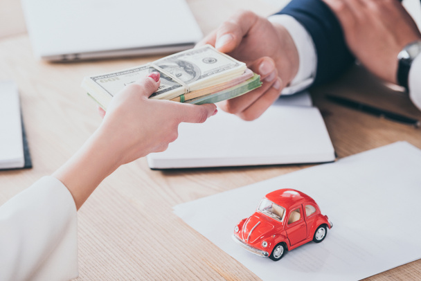 обрезанный снимок клиента, дающего деньги бизнесмену возле красной игрушечной машины на столе
 - Фото, изображение
