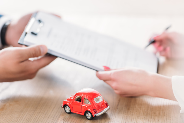 partial view of car dealer giving clipboard to client near miniature car  - Foto, afbeelding