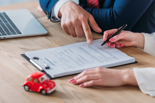 περικομμένη θέα της συμφωνίας αυτοκινήτου που δείχνει στο σημείο υπογραφής σε συμφωνία δανείου κοντά γυναίκα που κρατά στυλό - Φωτογραφία, εικόνα