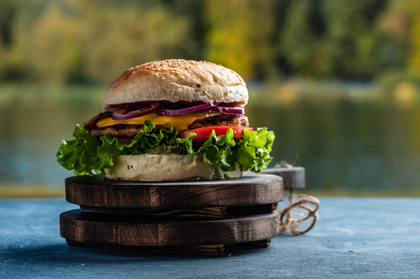 Juicy sabrosa hamburguesa con queso de res, lechuga, encurtidos, tomate y aros de cebolla en una mesa de madera. Comida callejera clásica - hamburguesa a la parrilla
. - Foto, Imagen