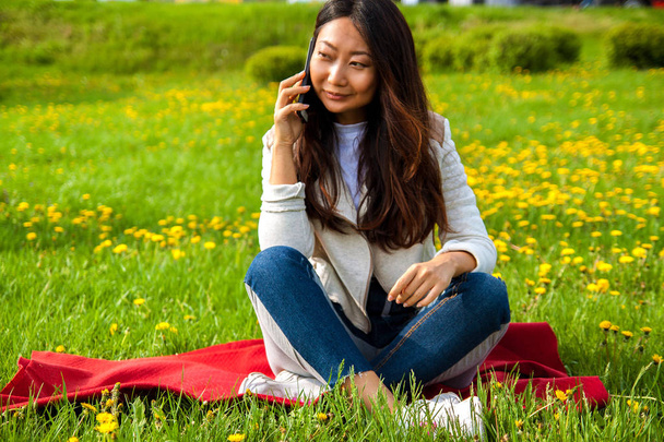 Ασίας ευτυχισμένη γυναίκα καλώντας το τηλέφωνο στο καλοκαιρινό πάρκο στο πράσινο γρασίδι. - Φωτογραφία, εικόνα
