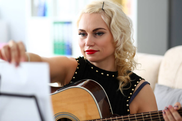 Mature blond woman turning notes pages while playing western acoustic guitar - Fotoğraf, Görsel
