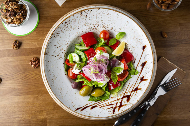 Греческий салат с сыром фета, оливками и травами, подается в белой тарелке на столе в ресторане, вид сверху
. - Фото, изображение