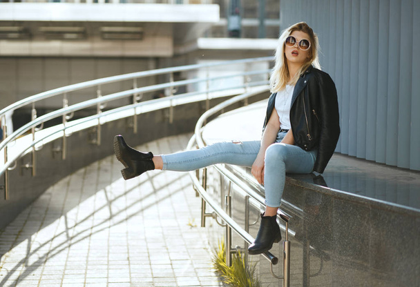 Fashionable stylish woman wearing jeans and jacket sitting on st - Zdjęcie, obraz