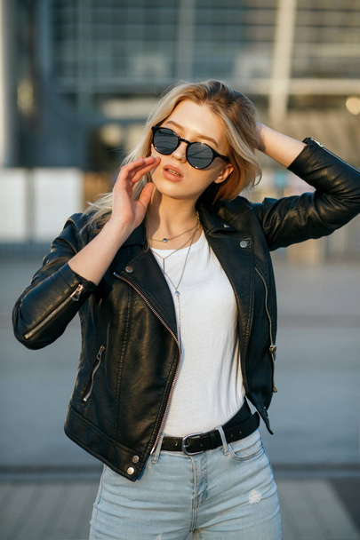Street shot of young stylish girl wearing sunglasses and black j - Foto, afbeelding