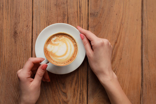 Gros plan mains féminines tenant tasse avec cappuccino café avec mousse avec un joli motif. Manucure parfaite de gel rouge poli. Table vintage bois naturel. Couleur créative post-traitement chaud
 - Photo, image