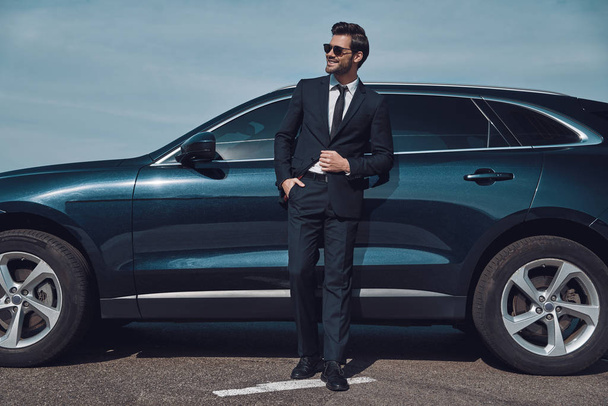 Great sense of style. Full length of handsome young businessman smiling while standing near his car outdoors - Fotó, kép