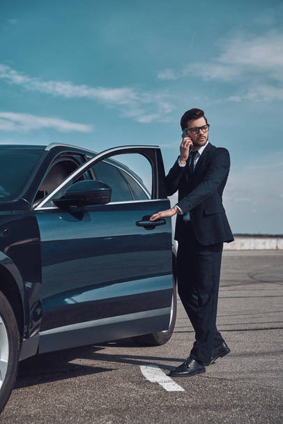 I will be in time! Full length of handsome young businessman talking on the phone while entering his car outdoors - Photo, Image