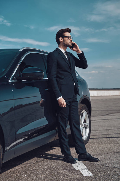 Talking about business. Full length of handsome young businessman talking on the phone while standing near his car outdoors - Photo, Image