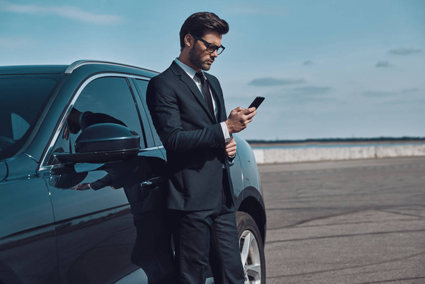 Portrait of confidence. Handsome young businessman using smart phone while standing near his car outdoors - Fotoğraf, Görsel