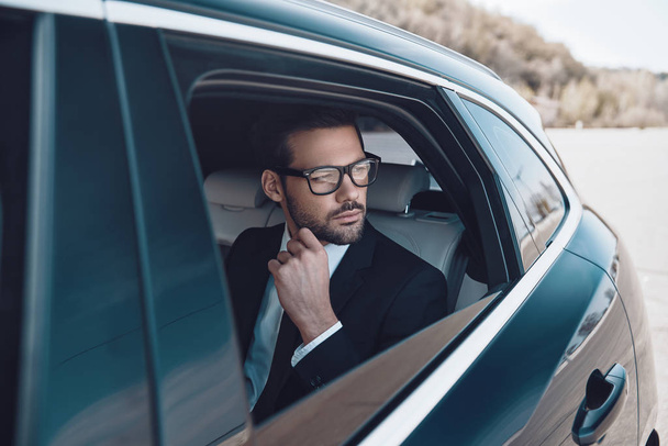 Thinking about. Thoughtful young businessman keeping hand on chin while sitting in the car             - 写真・画像