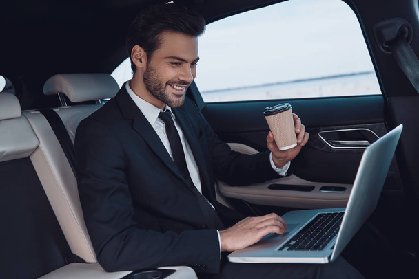 Always in touch. Handsome young man in full suit working using laptop while sitting in the car - 写真・画像