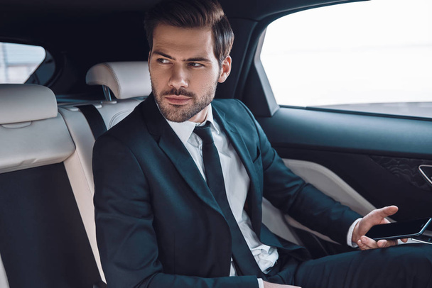 Young and successful. Handsome young man in full suit looking away while sitting in the car  - Zdjęcie, obraz