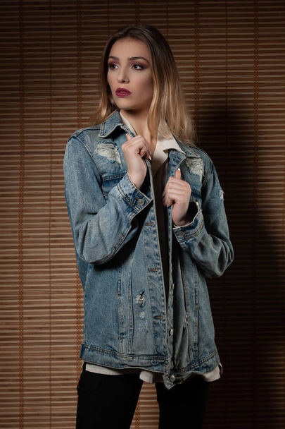Beautiful young woman in jeans jacketover bamboo wall in backgro - Foto, imagen