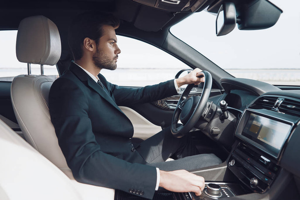 Time is money. Handsome young man in full suit looking straight while driving a car            - Foto, imagen