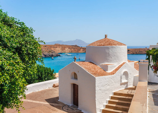 Vue sur la mer paysage photo baie et église orthodoxe à Lindos sur l'île de Rhodes, Dodécanèse, Grèce. Panorama avec belle plage de sable et eau bleue claire. Destination touristique célèbre en Europe du Sud
 - Photo, image