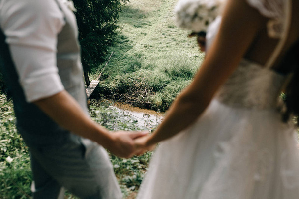 Schnappschuss eines schönen jungen Hochzeitspaares, das sich Händchen haltend in der Nähe von Bach steht - Foto, Bild