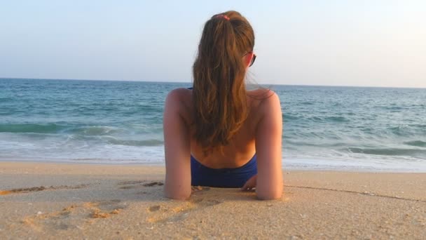 Giovane ragazza sdraiata sulla spiaggia e prendere il sole. Donna irriconoscibile che si rilassa sulla riva dell'oceano durante i viaggi di vacanza estiva. Concetto di riposo sulla costa del resort. Rallentatore Avvicinamento Retrovisore - Filmati, video