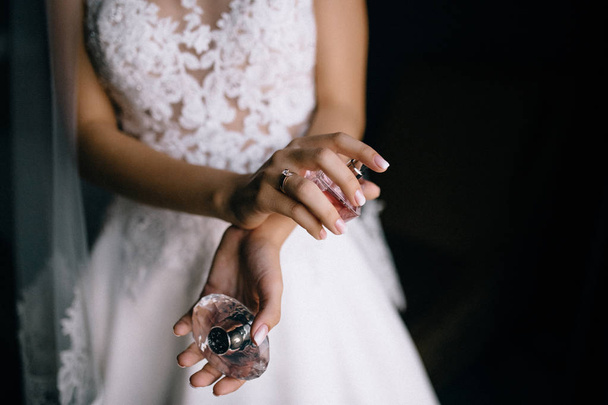 Mid τμήμα της νεαρής νύφης σε λευκό νυφικό κρατώντας το μπουκάλι άρωμα σε εσωτερικούς χώρους  - Φωτογραφία, εικόνα