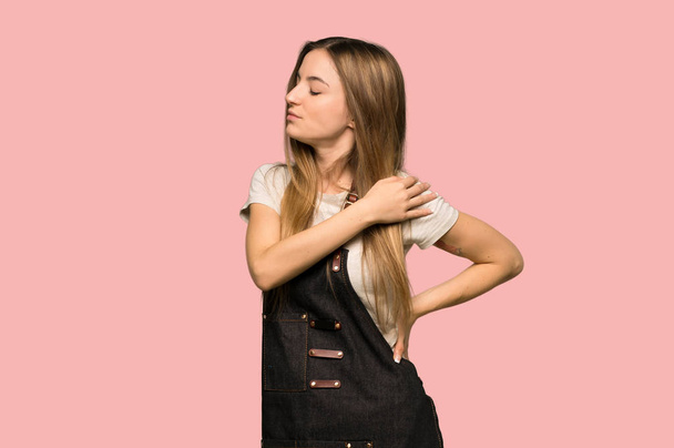 Giovane donna con grembiule che soffre di dolore alla spalla per aver fatto uno sforzo su sfondo rosa isolato
 - Foto, immagini