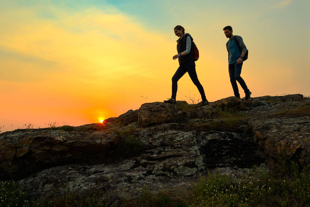 Young Happy Travelers Hiking with Backpacks on the Rocky Trail at Summer Sunset. Family Travel and Adventure Concept. - Photo, Image