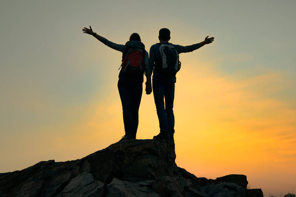 Couple de jeunes voyageurs avec sac à dos debout sur le sommet du rocher au coucher du soleil d'été. Concept de voyage et d'aventure
. - Photo, image