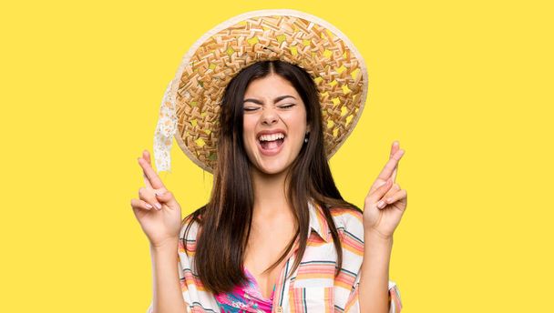 Teenager girl on summer vacation with fingers crossing over isolated yellow background - Photo, Image