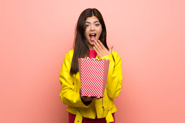 Teenager girl eating popcorns over pink wall - Fotó, kép
