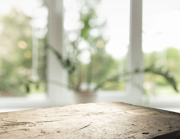 Mesa de madera en desenfoque de cristal de la ventana y verde abstracto del jardín con vista a la ciudad en el fondo de la mañana. Para la exhibición del producto de montaje
 - Foto, imagen