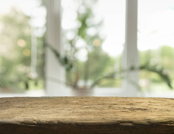Mesa de madera en desenfoque de cristal de la ventana y verde abstracto del jardín con vista a la ciudad en el fondo de la mañana. Para la exhibición del producto de montaje
 - Foto, Imagen