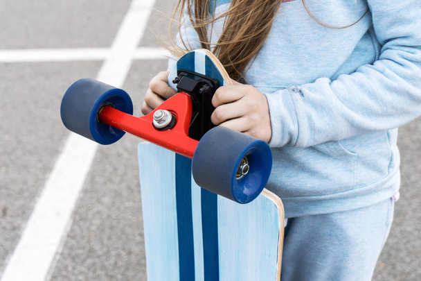 A girl in a blue jacket holding a large longboard. - Foto, afbeelding