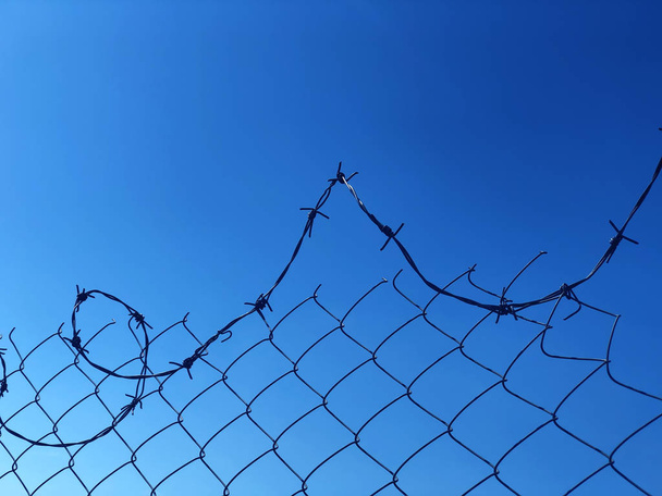 Fondo de una cerca de alambre de púas contra un cielo azul
  - Foto, Imagen