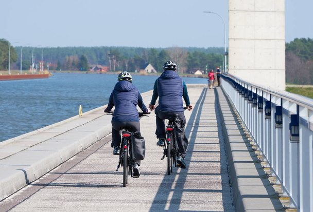 ドイツのホーエンワルテのエルベ川に架かるトラフ橋を渡る2人のサイクリスト - 写真・画像