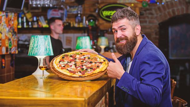 Hipster client sit at bar counter. Man received delicious pizza. Enjoy your meal. Cheat meal concept. Pizza favorite restaurant food. Fresh hot pizza for dinner. Hipster hungry eat italian pizza - Foto, Bild