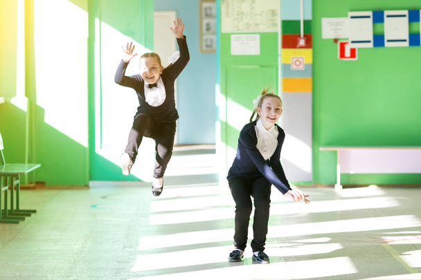 Liseli kızlar koridorda koşuşturarak oynarlar. Kız öğrenciler okul tatilinde birlikte koşarak eğlenirler. - Fotoğraf, Görsel