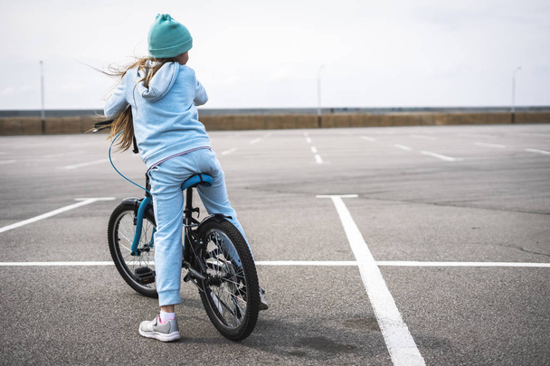 A girl in a hat and a blue sweater on a bicycle stopped and looks around. - Photo, Image