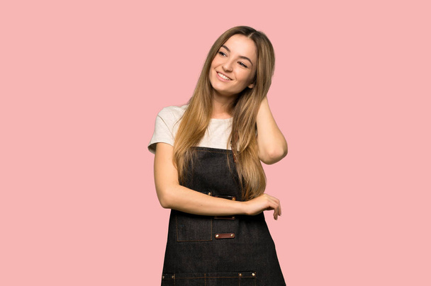 Young woman with apron thinking an idea while scratching head on isolated pink background - Foto, Bild