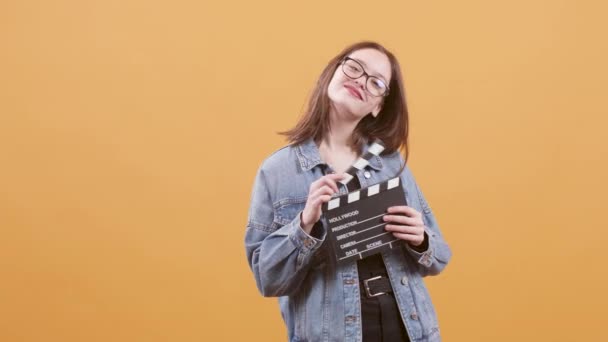 Beautiful teenage girl hold a clapperboard and smiles to the camera - Materiaali, video