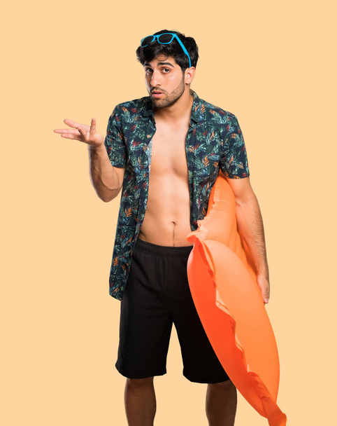 Man in trunks making doubts gesture over isolated yellow background - Photo, Image