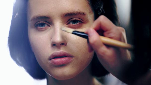 vista parcial del artista de maquillaje aplicando la base de la cara en la cara modelo con cepillo cosmético
 - Metraje, vídeo