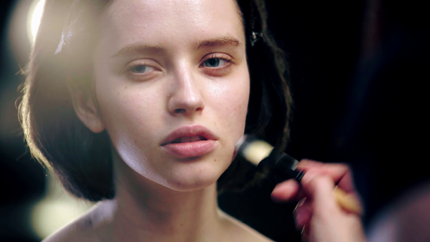 częściowy widok makijażu artysty stosowania podkładu na twarz modelu z pędzlem kosmetycznym - Materiał filmowy, wideo