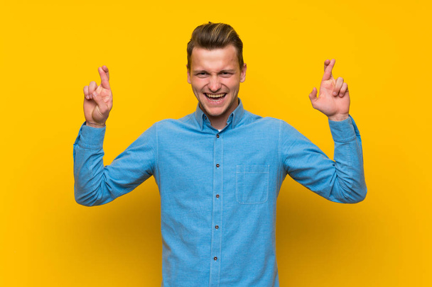 Homme blond sur mur jaune isolé avec les doigts croisés
 - Photo, image