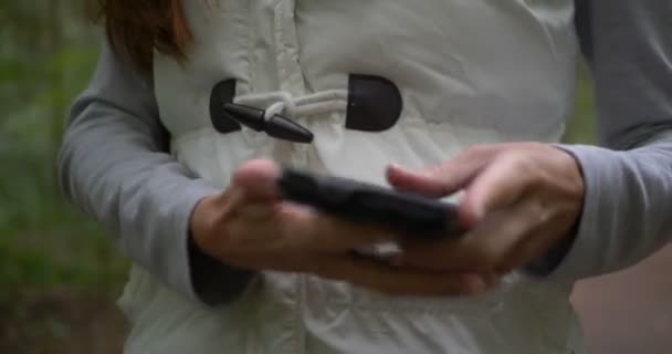 Młoda kobieta otwiera smartfona, aby szukać informacji w lesie wiosną - Materiał filmowy, wideo