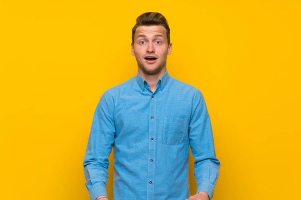 Ξανθιά άνδρα πάνω σε μια απομονωμένη κίτρινο τοίχο με έκπληξη του προσώπου έκφραση - Φωτογραφία, εικόνα