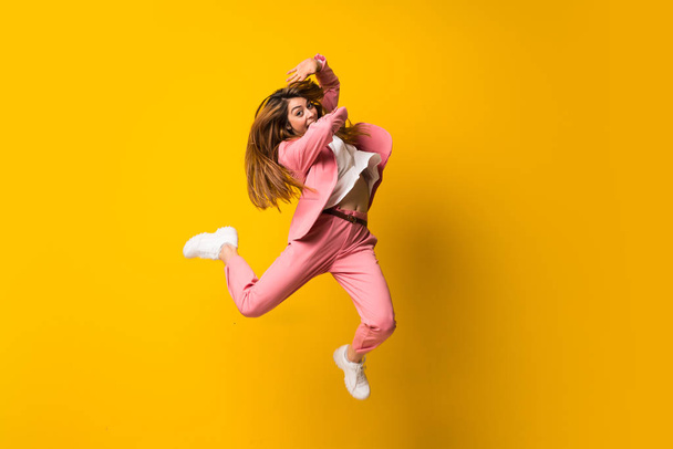 Young woman jumping over isolated yellow wall - Foto, Imagen