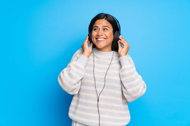 Young Colombian girl with sweater listening to music with headphones - Photo, image