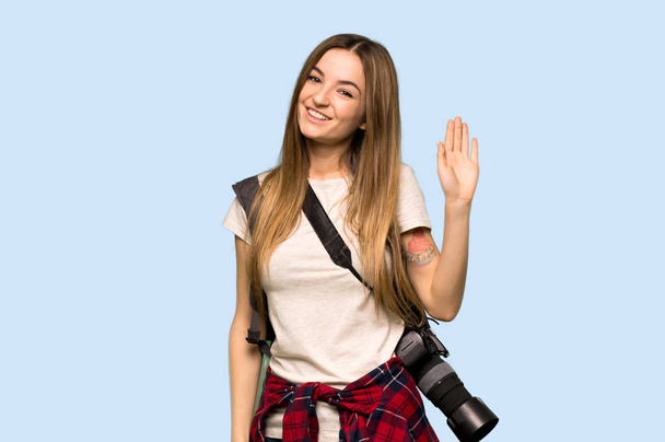 Genç fotoğrafçı kadın mavi arka planda mutlu bir ifadeyle selamlıyor. - Fotoğraf, Görsel